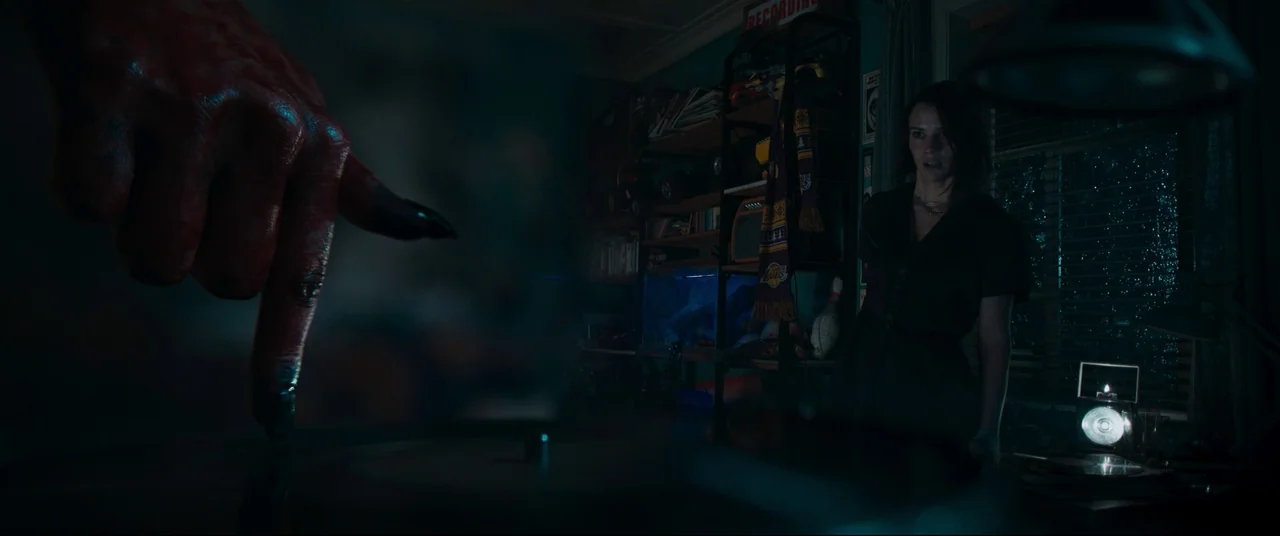 Evil Dead Rise (2023) movie still: medium — A dimly lit room contains a turntable, a bookshelf with miscellaneous items, and a window. A woman…