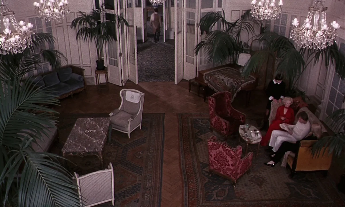Daughters of Darkness (1971) movie still: wide — A spacious hotel lobby features parquet wood floors, large potted palms, and crystal chandeliers. A…