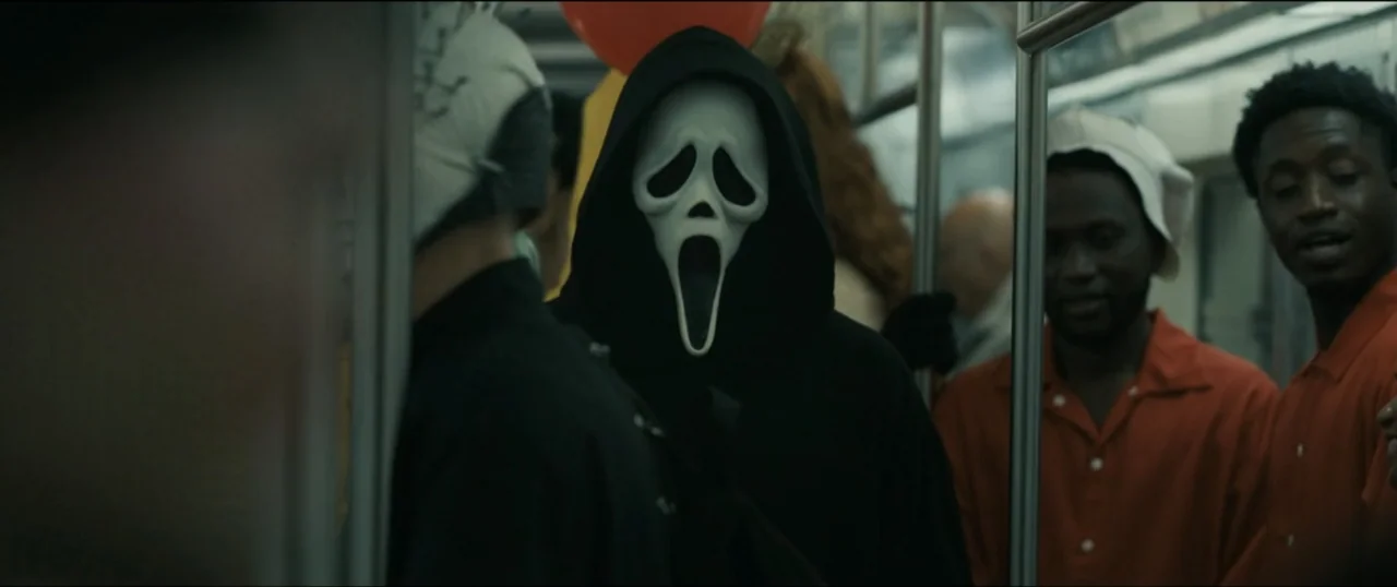 Scream VI (2023) movie still: medium — A crowded subway car interior features passengers standing near metal handrails and poles. A figure wearing a…