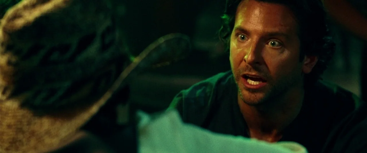 The Hangover Part III (2013) movie still: medium — A dark indoor space is filled with green ambient light and heavy shadows. A man with disheveled…