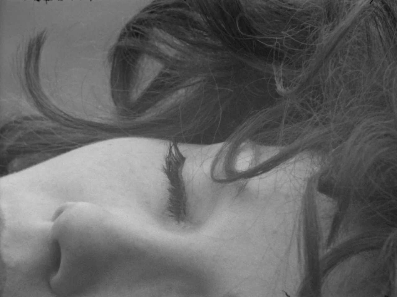A Woman Kills (1968) movie still: closeup — The frame captures a close-up of a person's face against a neutral background. Long dark hair is…