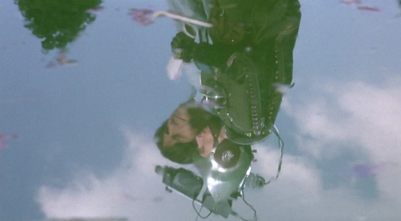 Kika (1993) movie still: medium — A reflection in a pool of water shows a person against a cloudy sky. The inverted image includes parts of the…