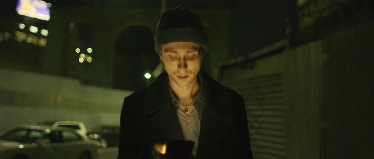 Depraved (2019) movie still: medium — A dimly lit parking lot at night with blurred city lights in the distance. A man stands in the center while…