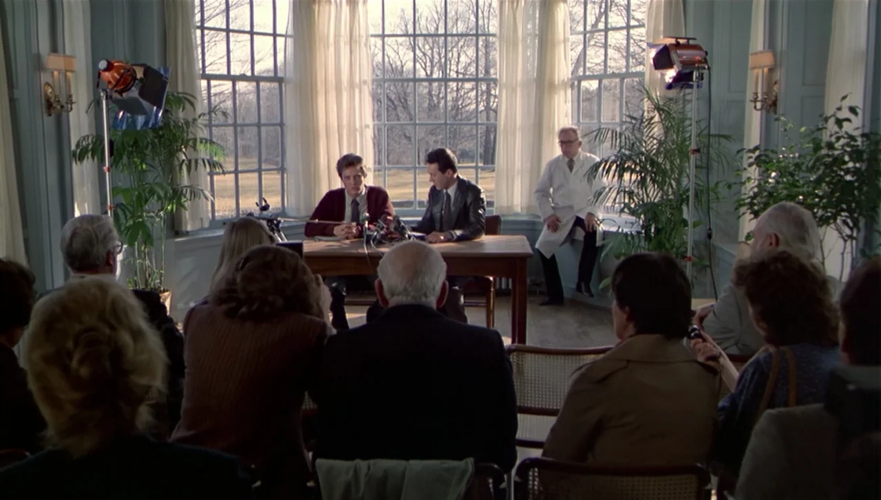 The Dead Zone (1983) movie still: wide — A bright room with a large window faces a bare landscape in late autumn. Two men sit at a central table…