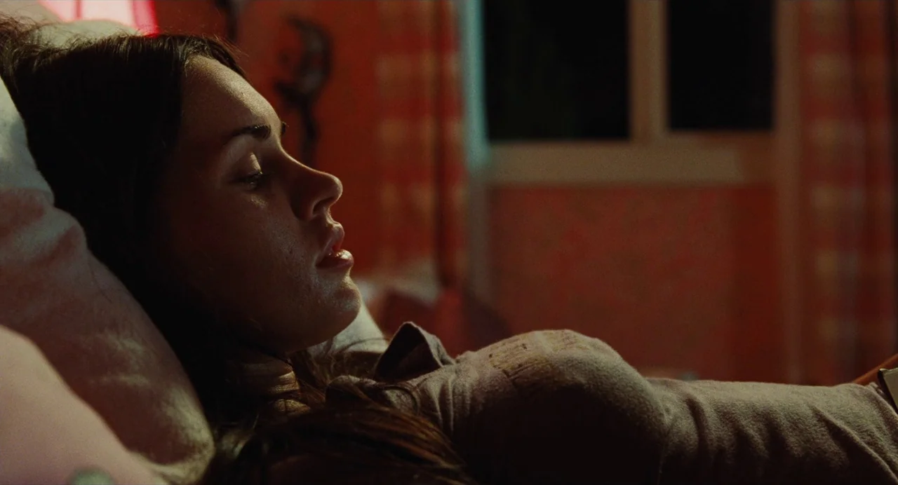 Jennifer’s Body (2009) movie still: closeup — A bedroom at night features warm lighting against a patterned wall and dark surroundings. A young…
