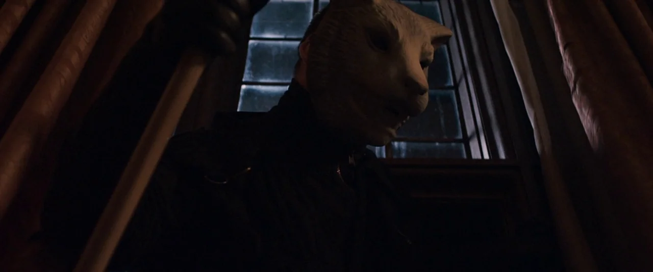 You’re Next (2013) movie still: medium — An interior space features a dark window framed by heavy fabric curtains. A masked figure stands in the…