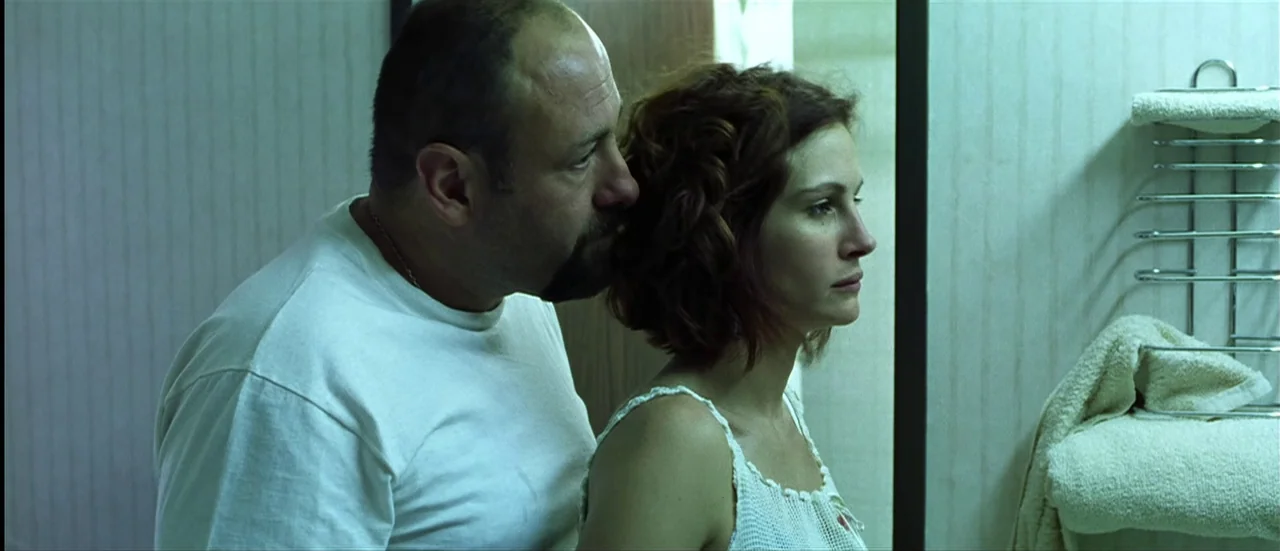 The Mexican (2001) movie still: medium — A cramped tiled bathroom contains a metal towel rack with folded white towels. A man whispers to a woman…