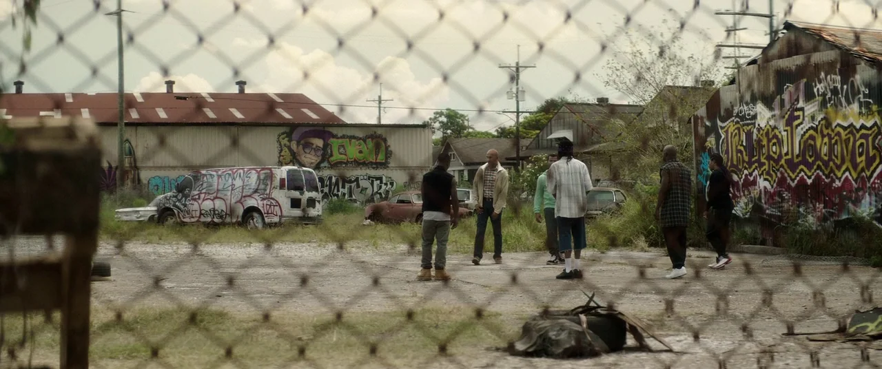 Keanu (2016) movie still: wide — A neglected urban lot features graffiti-covered corrugated metal structures and abandoned vehicles under overcast…