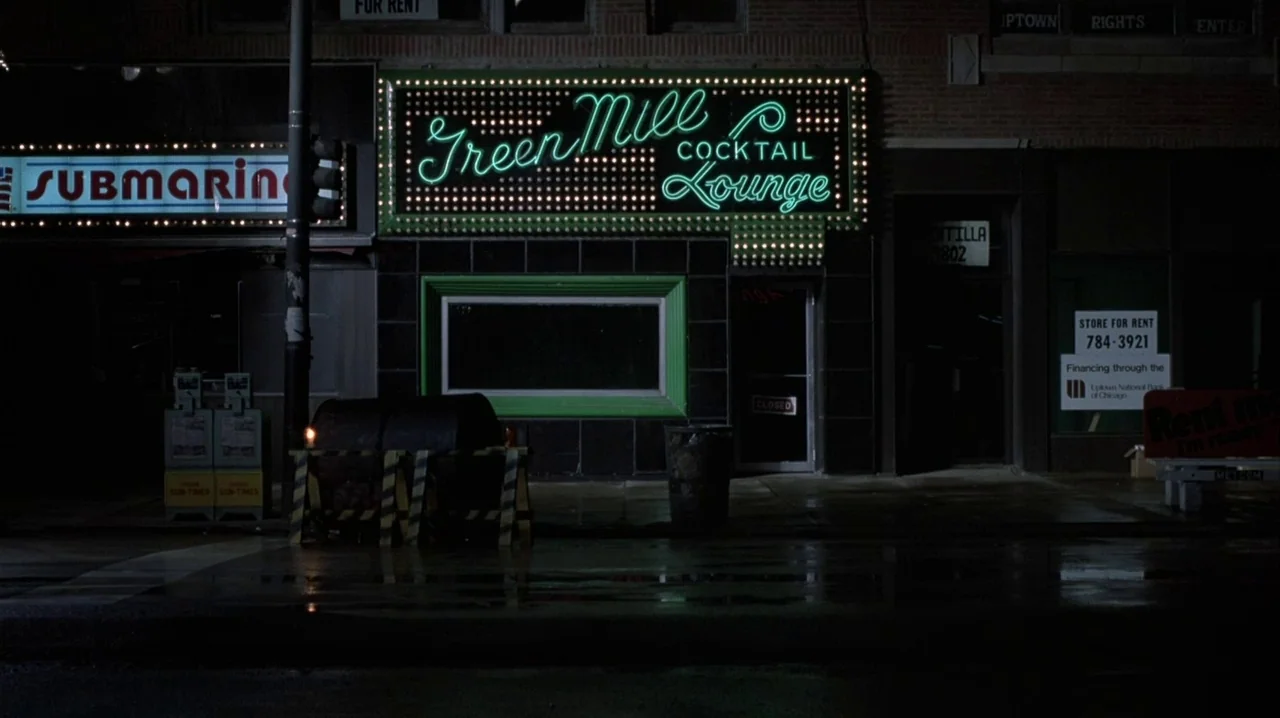 Thief (1981) movie still: wide — A nighttime view of a dark city street featuring a Green Mill neon sign. The sidewalk is empty and the storefront…