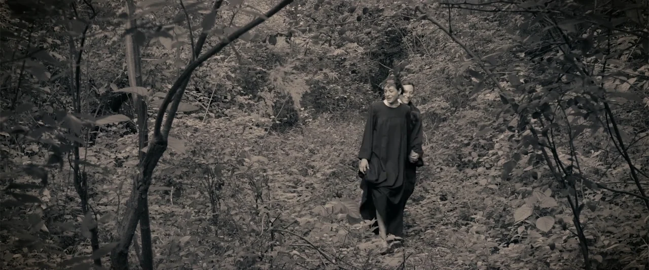 I Trust in You (2016) movie still: fullbody — A narrow dirt path is surrounded by heavy brush and thin tree trunks. Two women in long dark dresses…