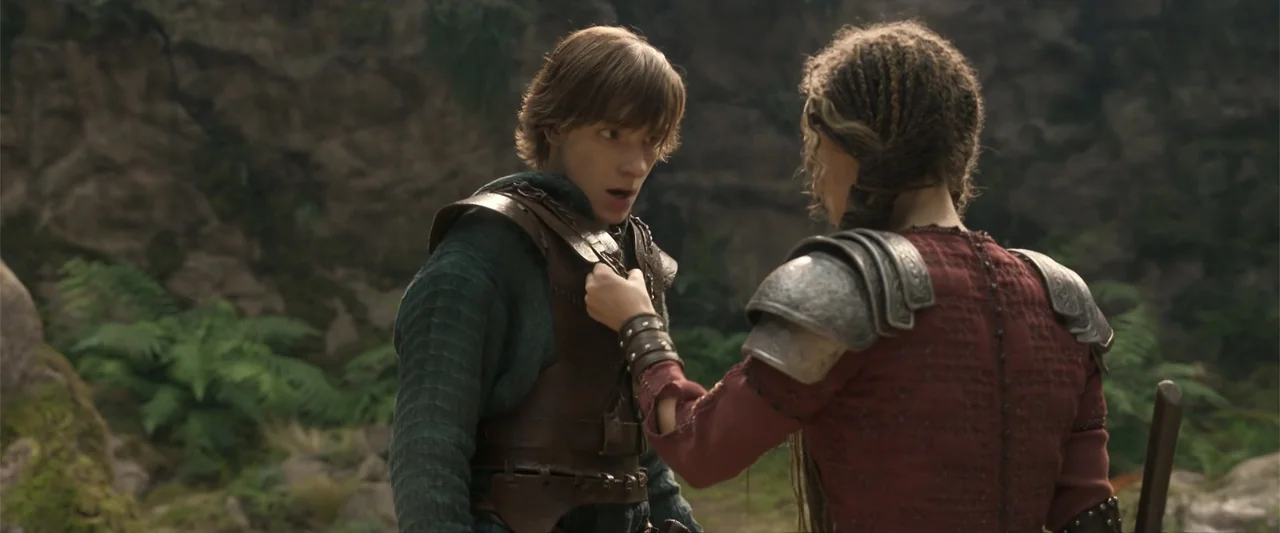 How to Train Your Dragon (2025) movie still: medium — A rocky, fern-covered outdoor area serves as the backdrop for two people in fantasy attire. A…