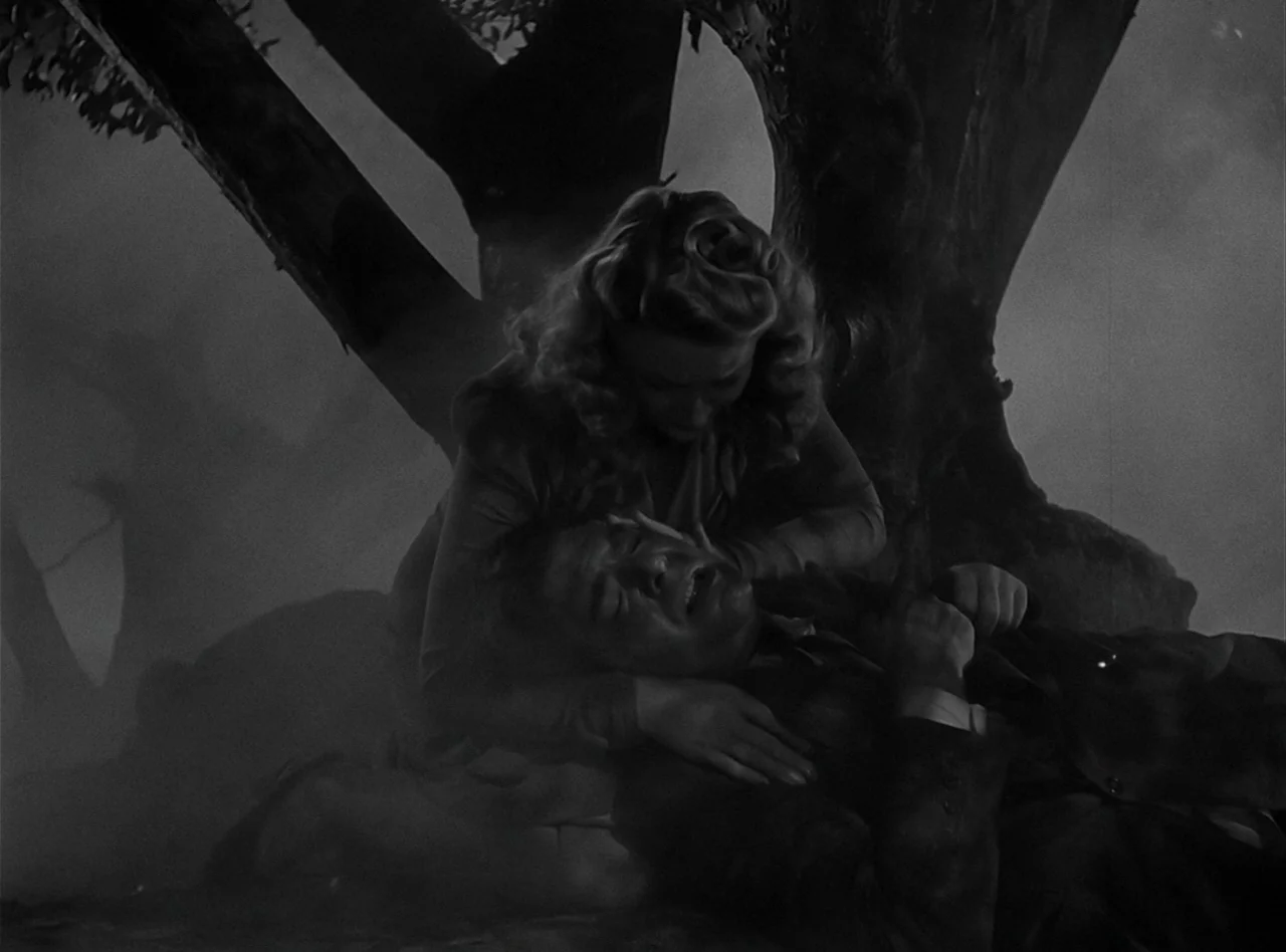 The Wolf Man (1941) movie still: medium — A dark, foggy clearing beneath the base of a large tree at night. A woman cradles a man's head on her lap…