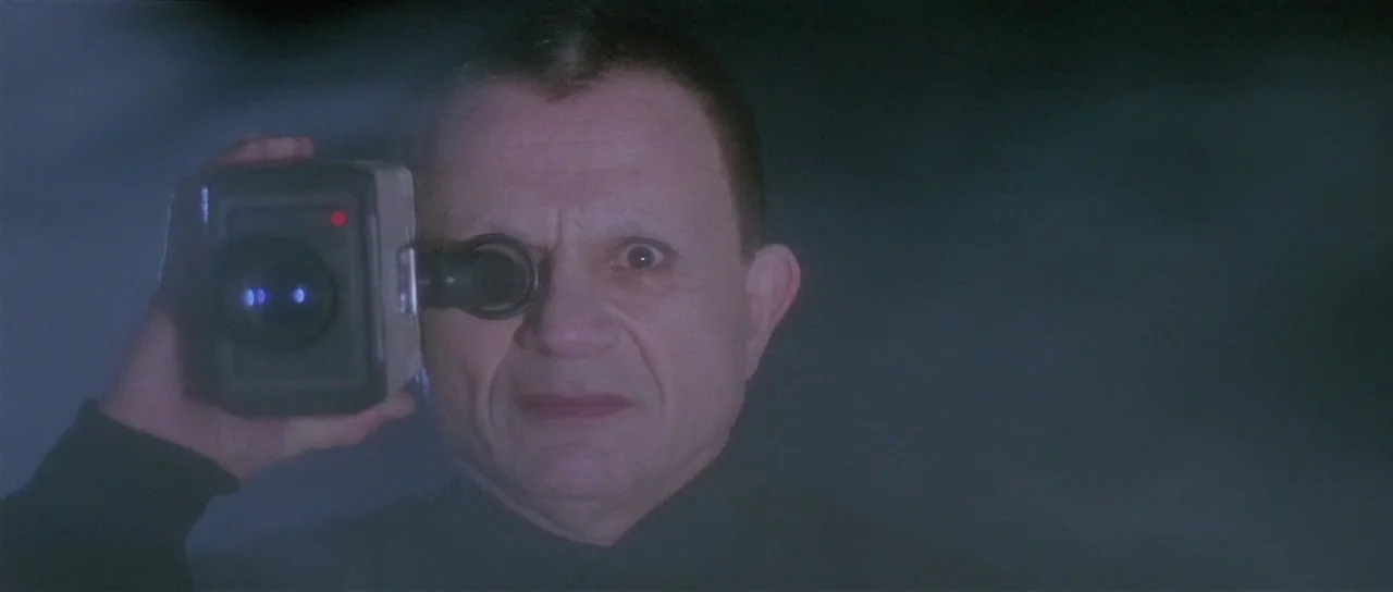 Lost Highway (1997) movie still: closeup — A man in a dark environment holds a camcorder close to his face. He peers through the small electronic…