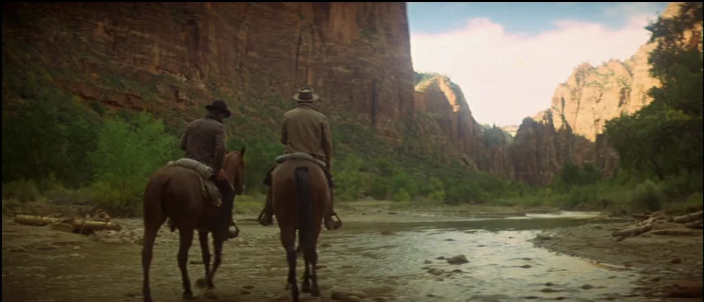 Butch Cassidy and the Sundance Kid (1969) movie still: wide — Two men on horseback cross a shallow river bed between towering red rock canyon walls.…