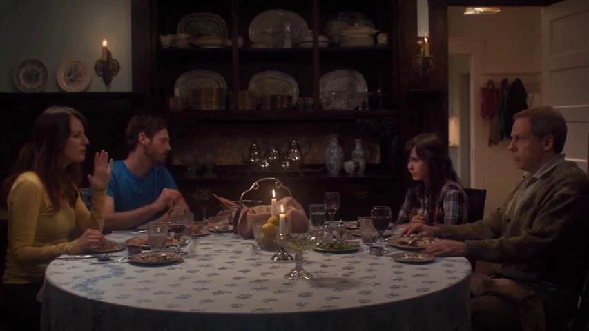 Touchy Feely (2013) movie still: medium — A dimly lit room contains a round table with a blue floral tablecloth. Four adults sit around the table…