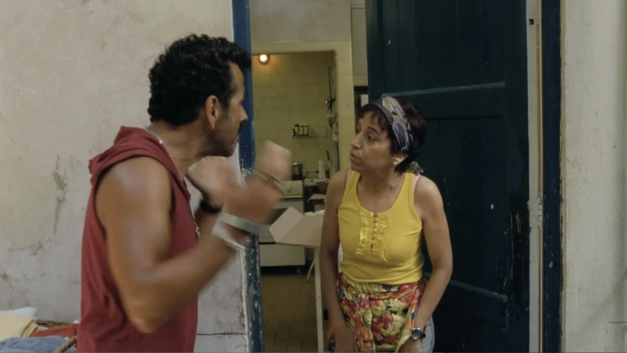 For Sale or Rent (2013) movie still: medium — A residential room features a dark blue doorway leading to a kitchen area. A man and a woman face each…