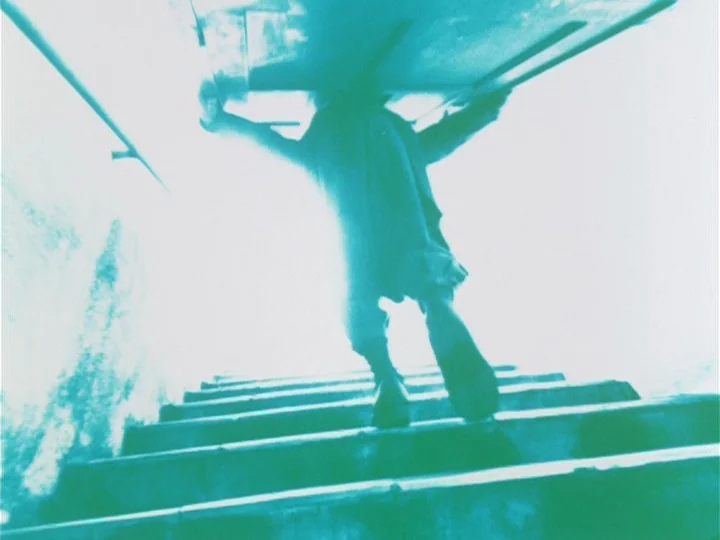 Labyrinth Tale (1975) movie still: fullbody — A concrete stairwell leads toward a bright opening at the top of the frame. A person in a long coat…