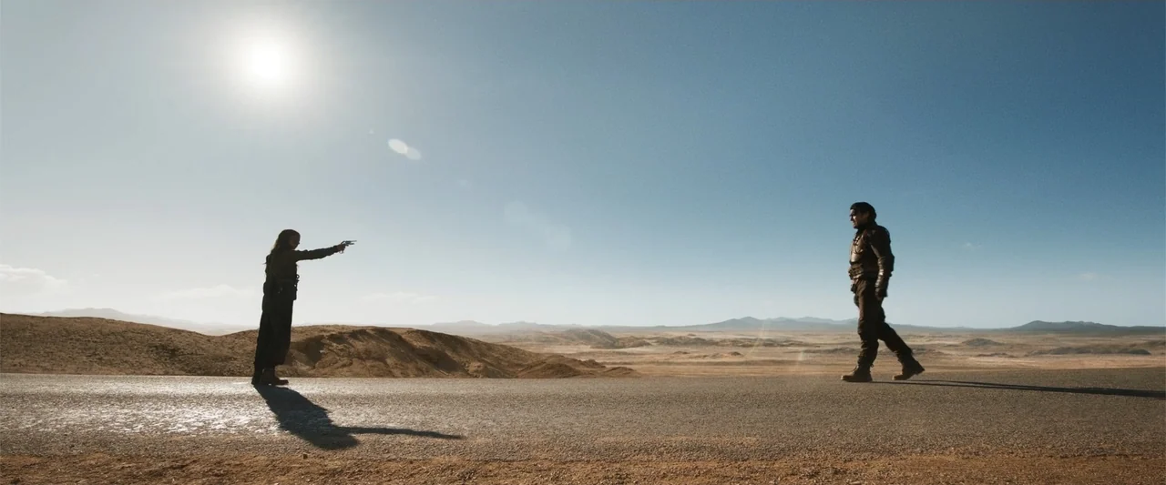 Furiosa: A Mad Max Saga (2024) movie still: wide — An asphalt road stretches across an arid, sun-bleached desert under a clear blue sky. A woman…