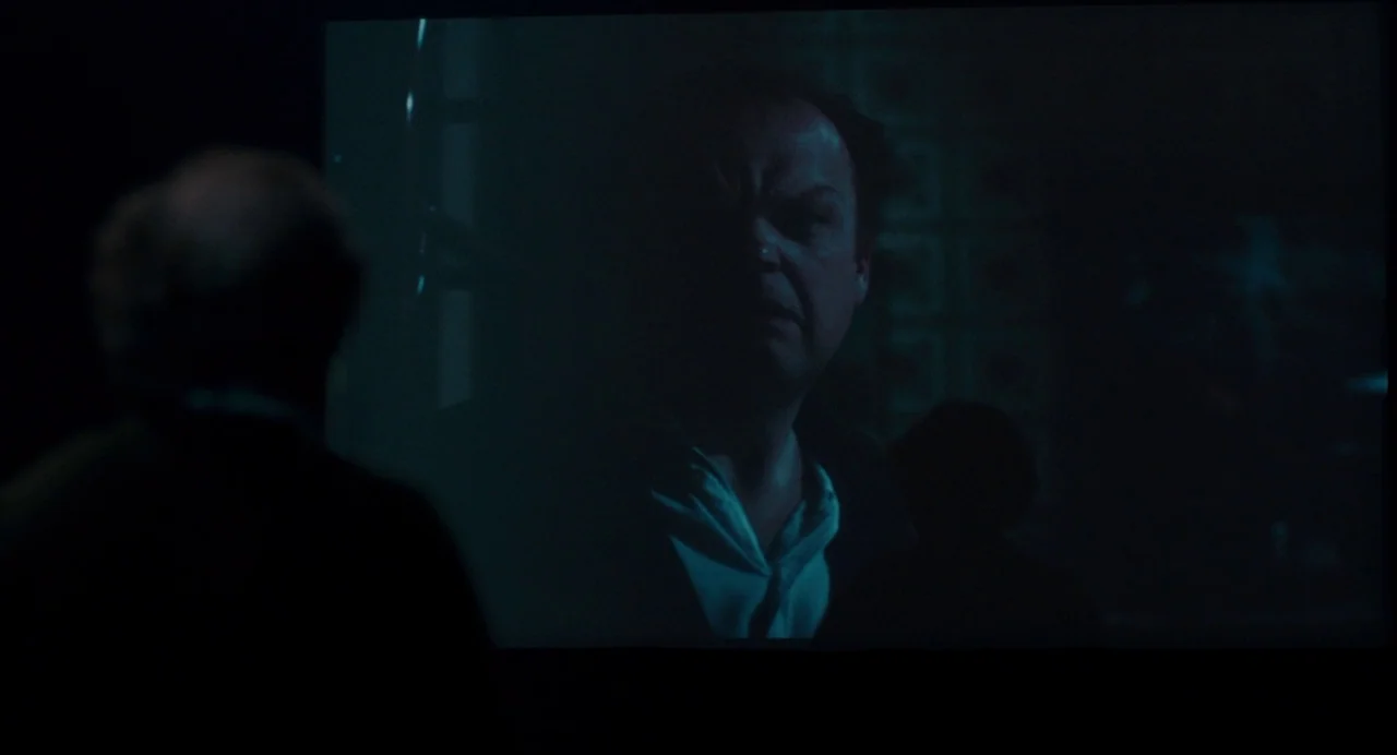 Berberian Sound Studio (2012) movie still: medium — A dark space features a large projection screen displaying a man in a shirt. An out-of-focus…