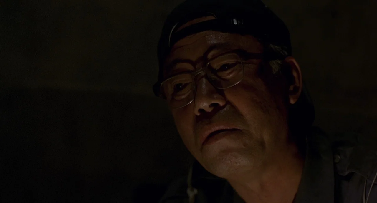 Barking Dogs Never Bite (2000) movie still: closeup — An older East Asian man is positioned against a dark, undefined background. He wears a…