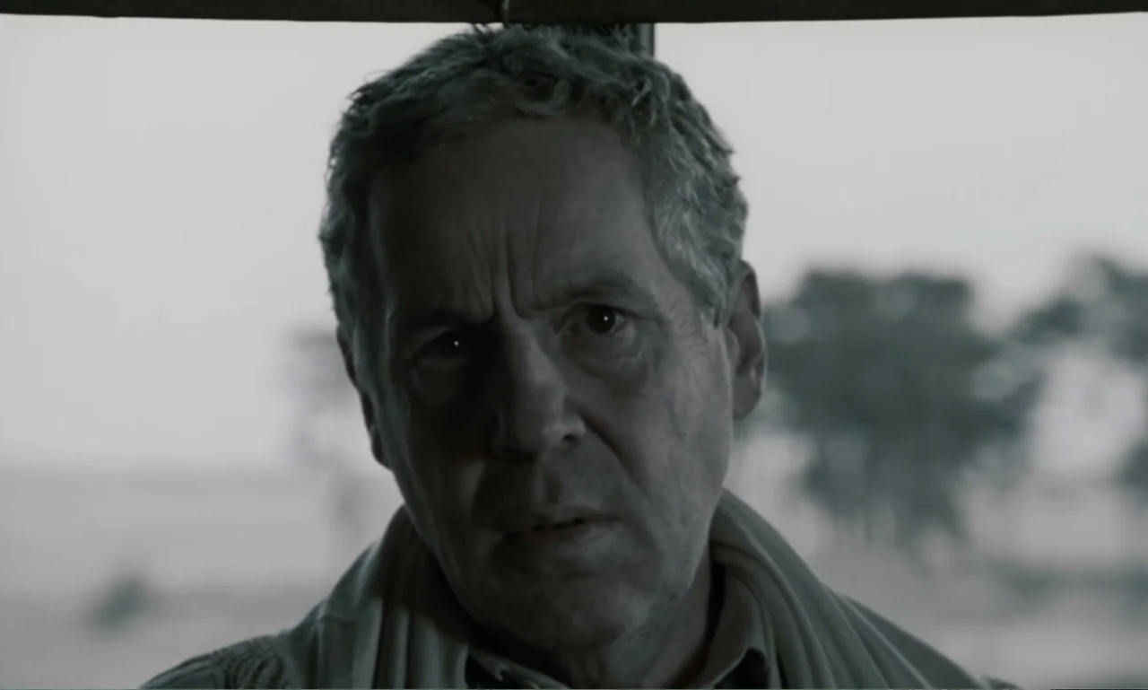 The Sacrifice (2015) movie still: closeup — An interior of a vehicle with a blurred outdoor environment visible in the distance. A middle-aged man…