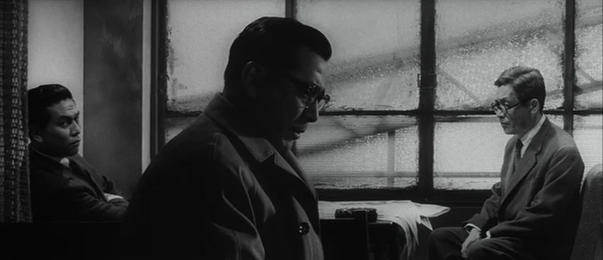 The Bad Sleep Well (1960) movie still: medium — A cramped train car with frosted windows showing a blurred landscape outside. Three men sit in…