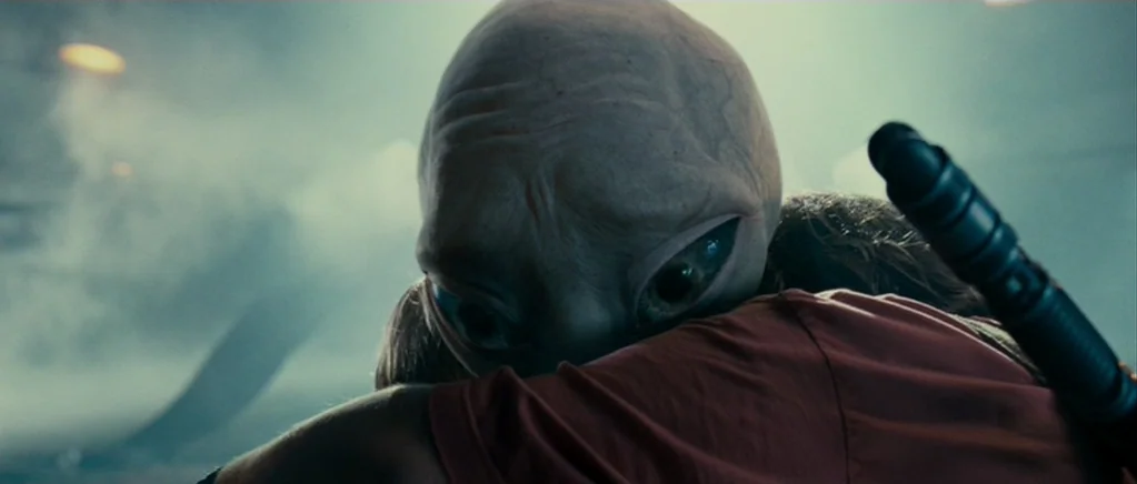 Paul (2011) movie still: closeup — A dark industrial space filled with thick smoke and dim light sources. A large-headed creature leans its face…