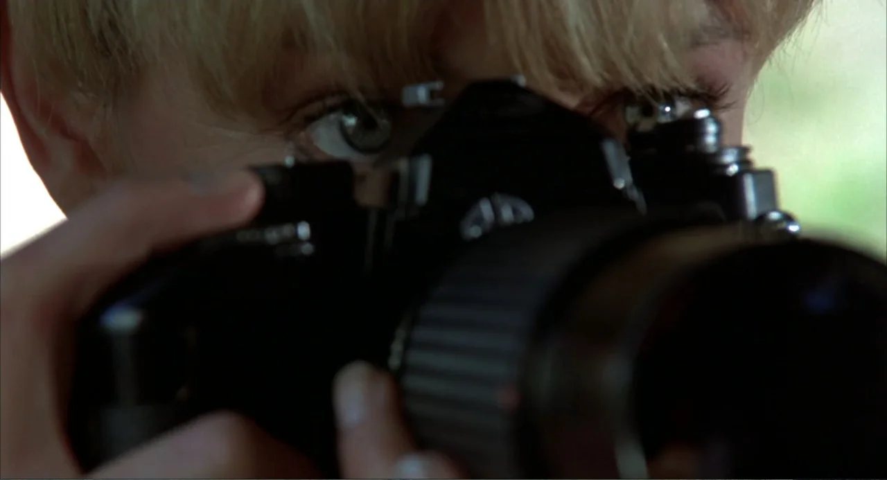 Murphy's Law (2009) movie still: closeup — A close-up view shows a person holding a large black professional camera. The subject peers through the…