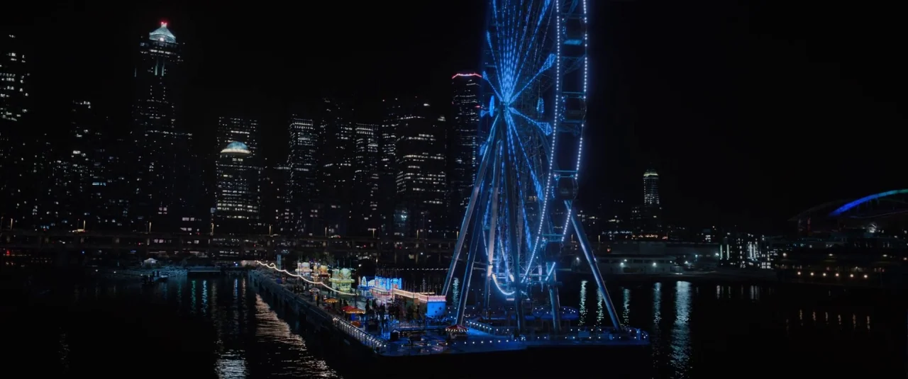 Death Note (2017) movie still: establishing — A night view shows a brightly illuminated Ferris wheel situated at the end of a long pier. Behind the…