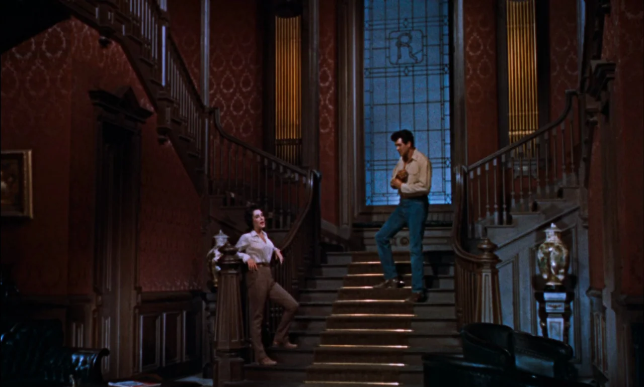 Giant (1956) movie still: wide — An opulent Victorian-style foyer features a large central staircase with elaborate wooden balustrades. A young man…
