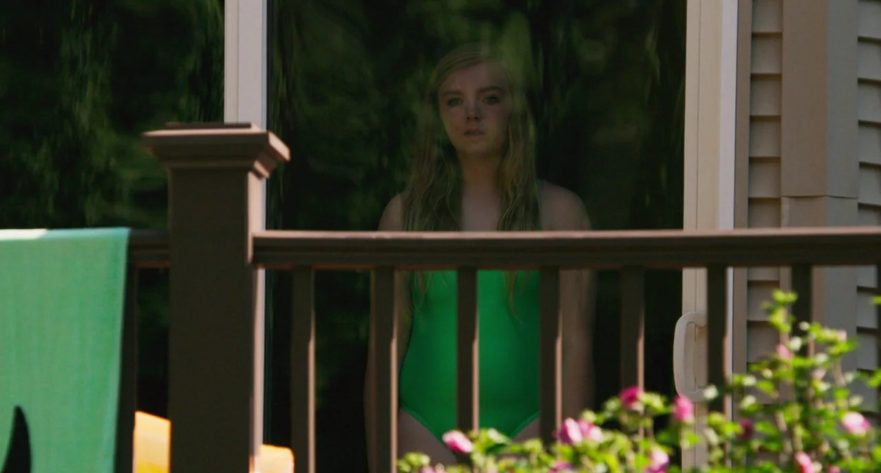 Eighth Grade (2018) movie still: medium — A woman stands behind a glass sliding door on a sunny day. She is wearing a green swimsuit and faces…