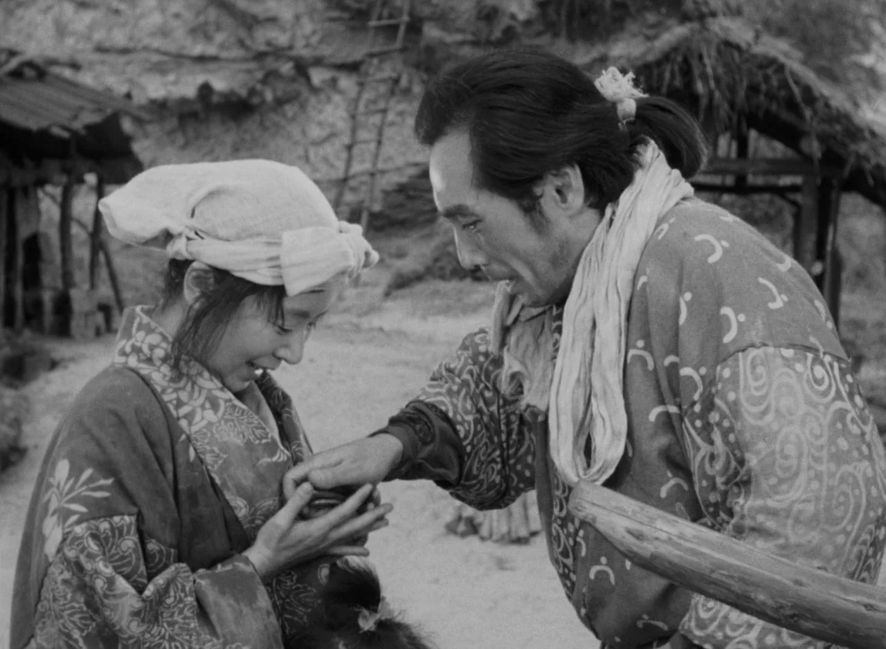 Ugetsu (1953) movie still: medium — A rural setting with dirt ground and rustic wooden structures in the background. A man hands a small object to a…