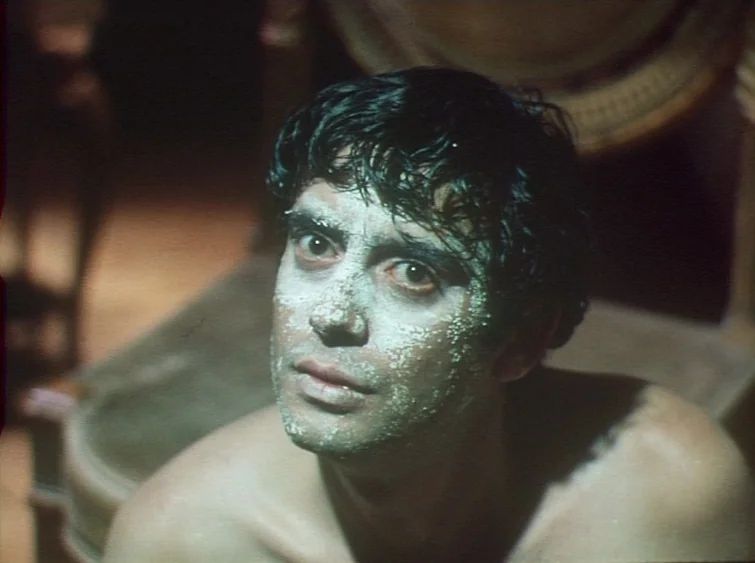 Hermitage (1968) movie still: closeup — A dimly lit interior space features a man with white powder on his face. He looks upward with a wide-eyed…
