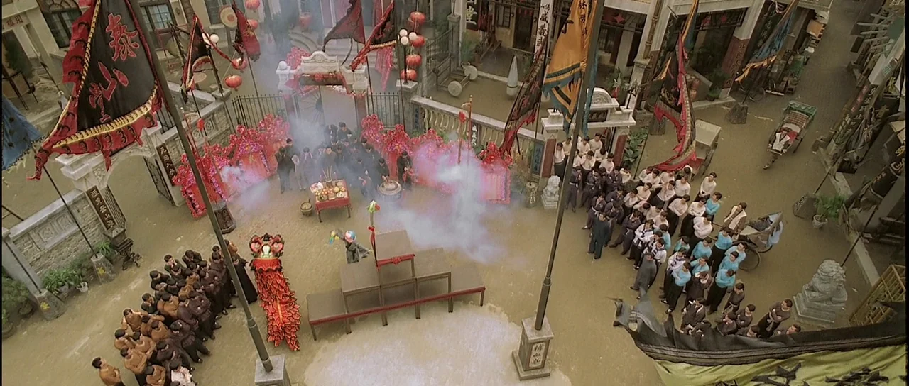 Ip Man (2008) movie still: wide — An open stone courtyard is decorated with Chinese festival flags and red ceremonial decor. A large crowd of people…