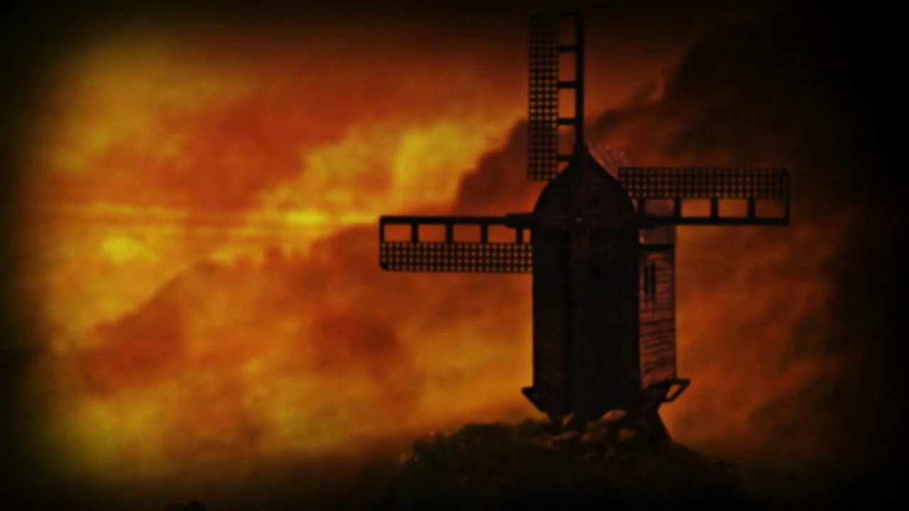 The Forbidden Room (2015) movie still: wide — A dark windmill silhouette sits atop a grassy hill against a vibrant orange sky. Dense orange and…