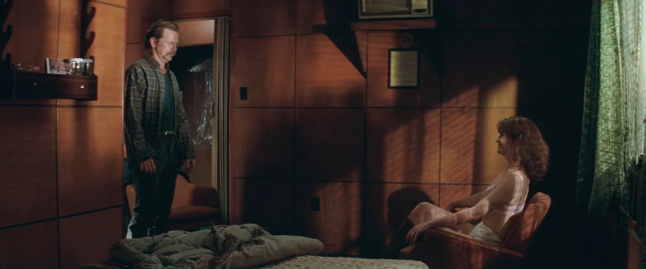 The Sweet Hereafter (1997) movie still: wide — A motel room features walls covered in square wood paneling and a worn bed. A man in a plaid shirt…