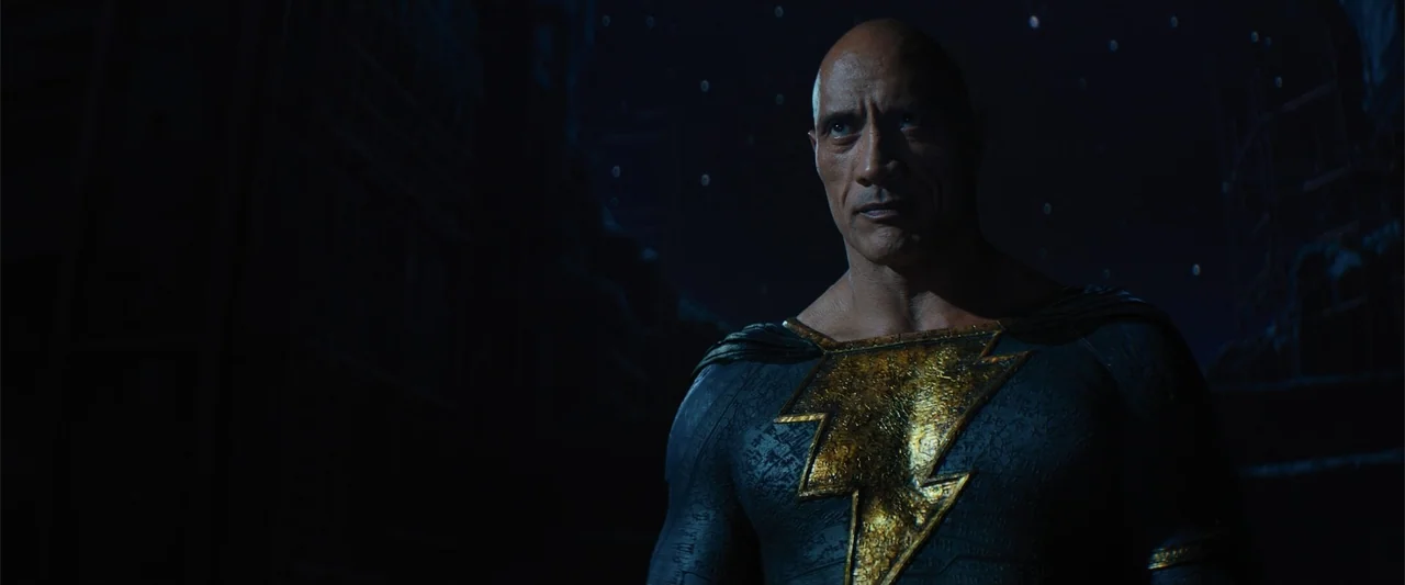 Black Adam (2022) movie still: medium — A dark, rocky area illuminated by cool blue night light under a starry sky. A muscular man wearing a black…