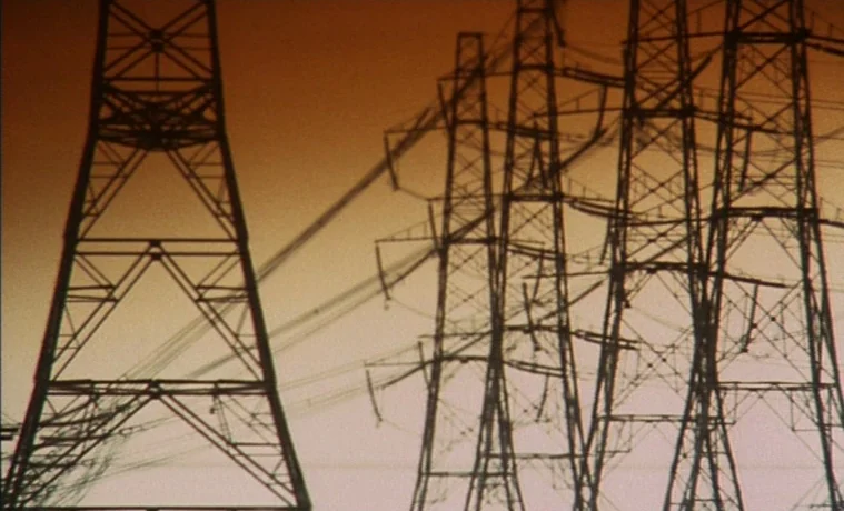 The Garden (1990) movie still: wide — Several tall steel electricity pylons stand against a vibrant sunset sky. The structures form dark, intricate…