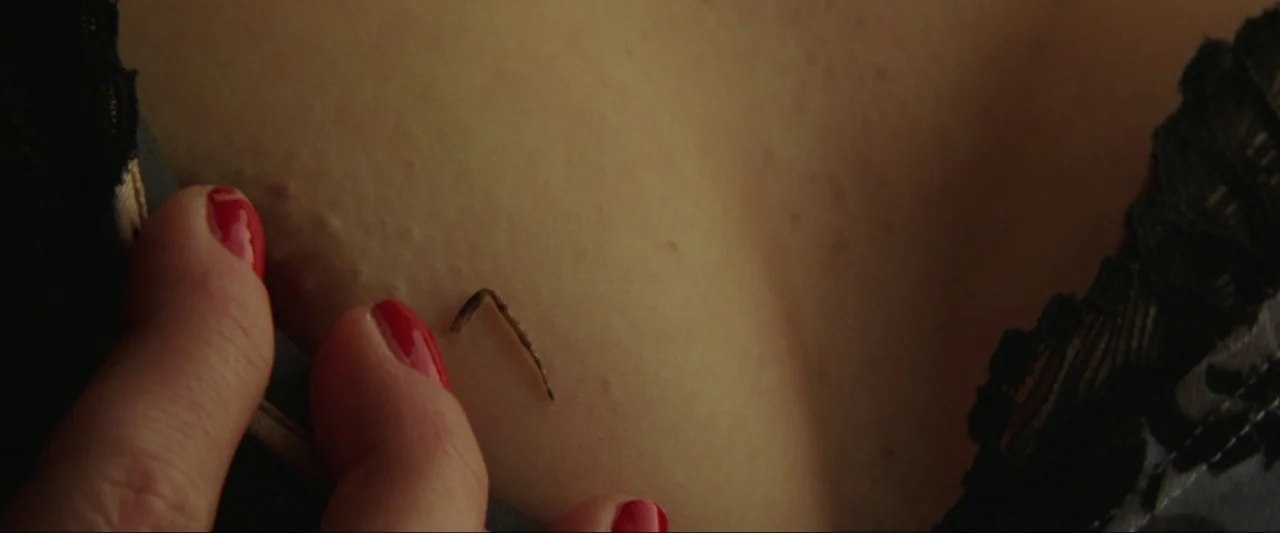 Kiss Kiss Bang Bang (2005) movie still: closeup — A close-up view of a person's chest area with black lace clothing visible. A hand with bright red…