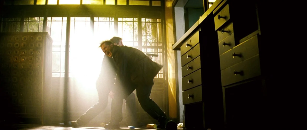 Mission: Impossible III (2006) movie still: medium — A dimly lit room with large wooden-framed windows letting in bright daylight. Two men are…