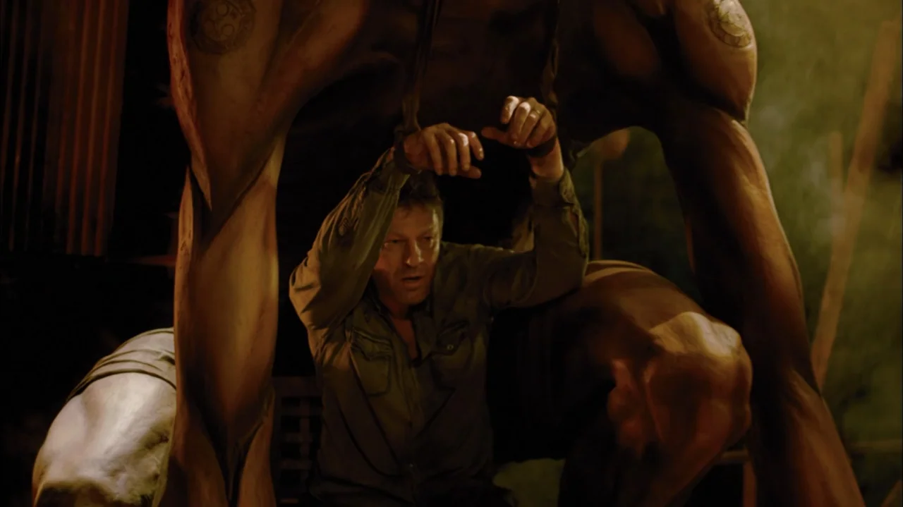 Silent Hill: Revelation 3D (2012) movie still: medium — A dimly lit room contains a large stone-like statue standing over a captured man. The man…