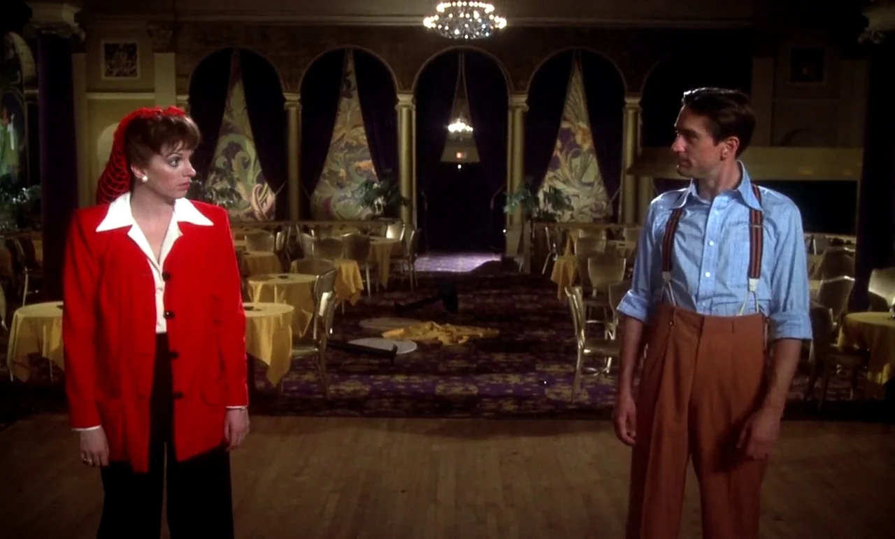 New York, New York (1977) movie still: fullbody — A spacious, dimly lit formal ballroom with violet curtains and tables covered in gold cloths. A…