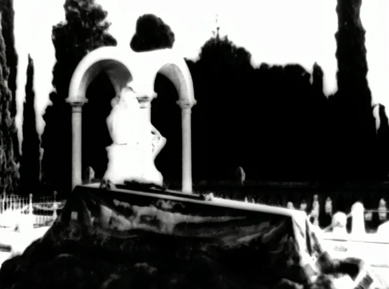 Cuadecuc, Vampir (1971) movie still: wide — A high-contrast cemetery scene features a stone funerary monument beneath an archway. Dense black trees…