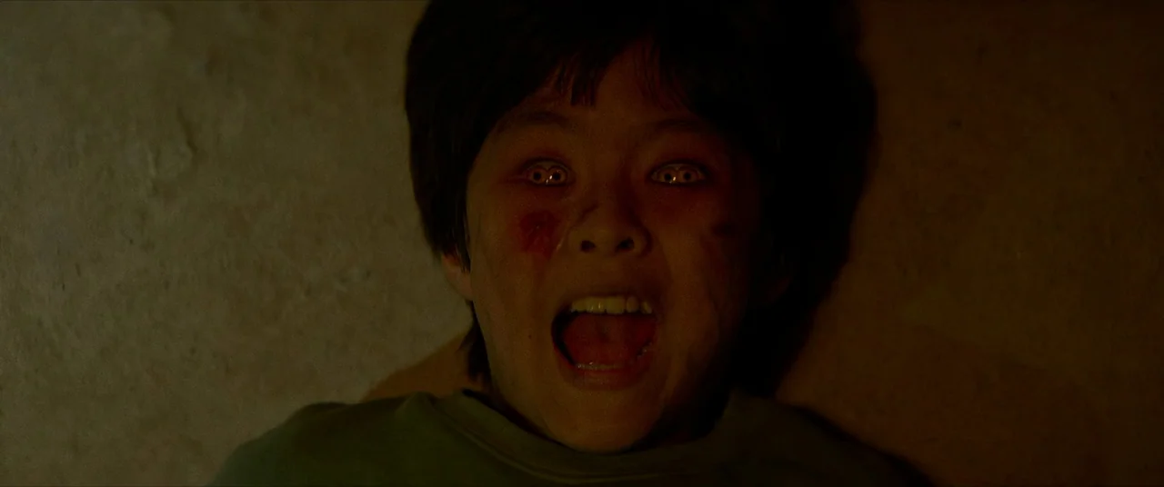 The Divine Fury (2019) movie still: closeup — A dark indoor setting with a warm, dim light source highlighting a subject. A young child lies on a…