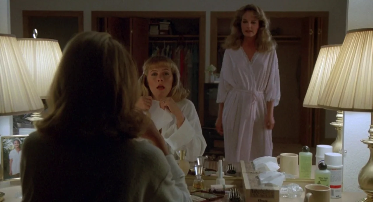 Peggy Sue Got Married (1986) movie still: medium — Two women stand in front of a wide vanity mirror in a brightly lit room. One woman sits at the…