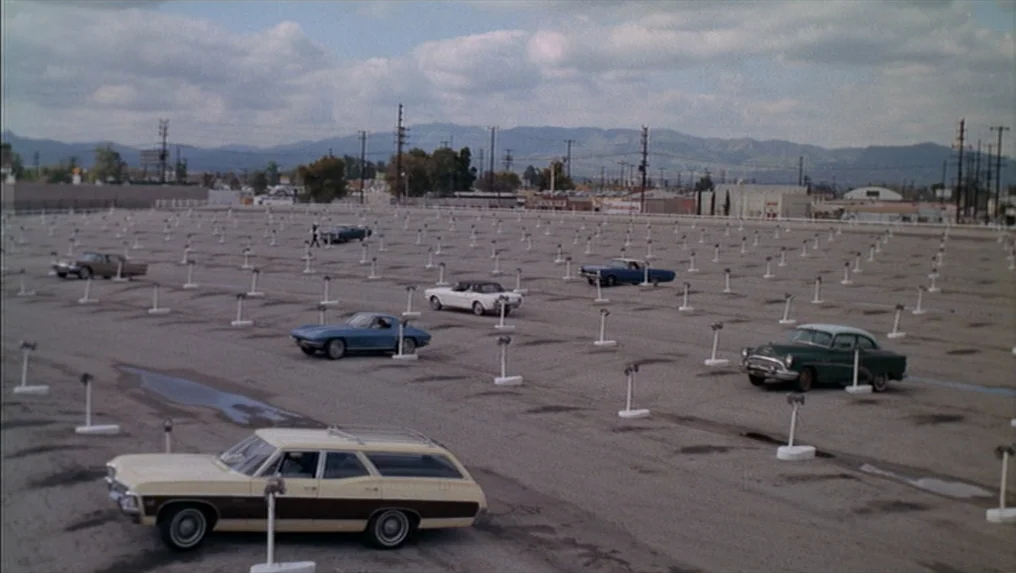 Targets (1968) movie still: wide — A vast, paved parking lot filled with spaced-out vintage automobiles under a cloudy sky. The rows of vehicles…