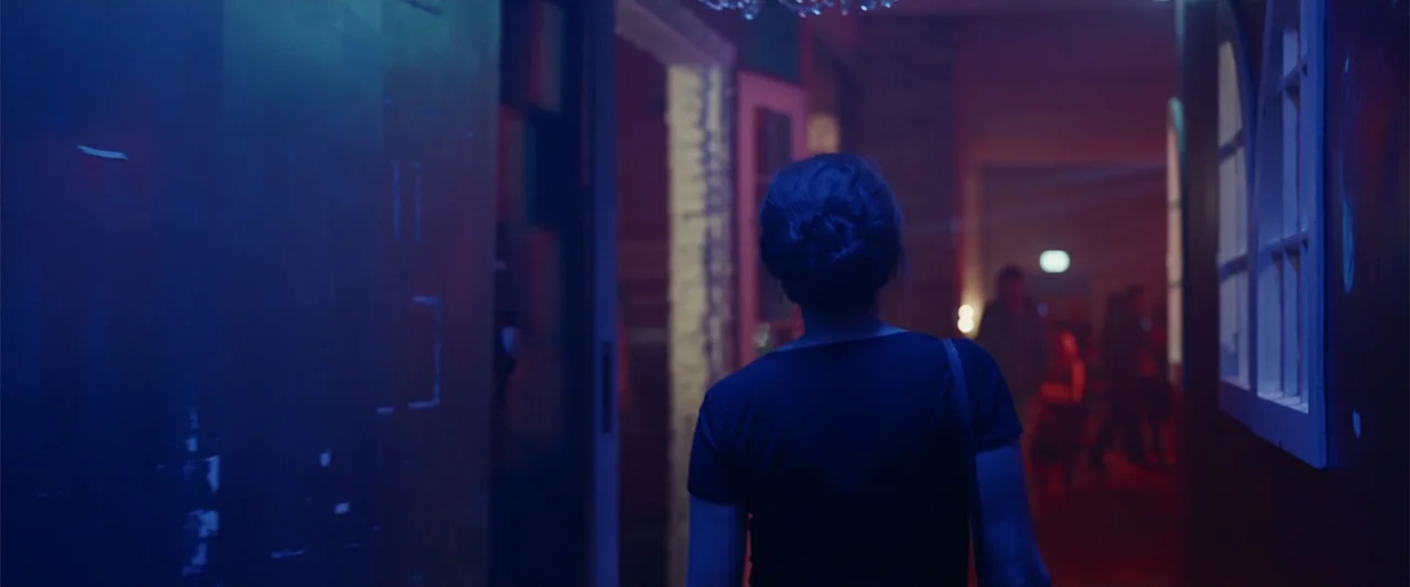 Beautiful Brazil (1952) movie still: medium — A narrow corridor features dark walls illuminated by vibrant blue and red neon lights. A woman in a…