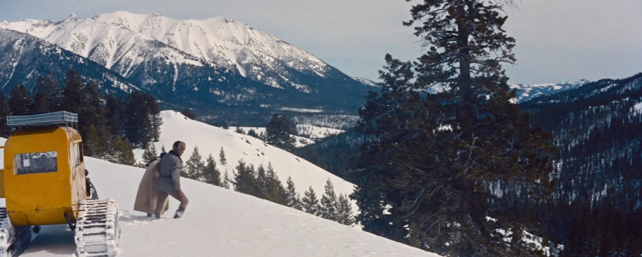 How to Marry a Millionaire movie still: wide — A bright snowy mountain slope is flanked by dense pine trees and distant peaks. Two people descend…