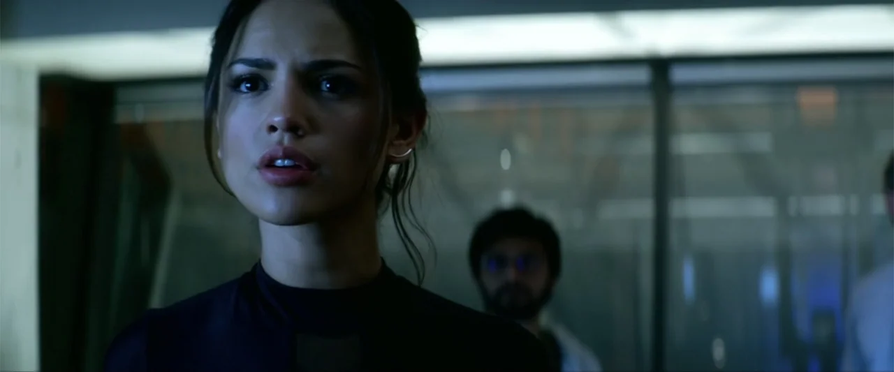 Bloodshot (2020) movie still: closeup — A dark office environment features a blurred glass partition in the background. A woman in a black shirt…