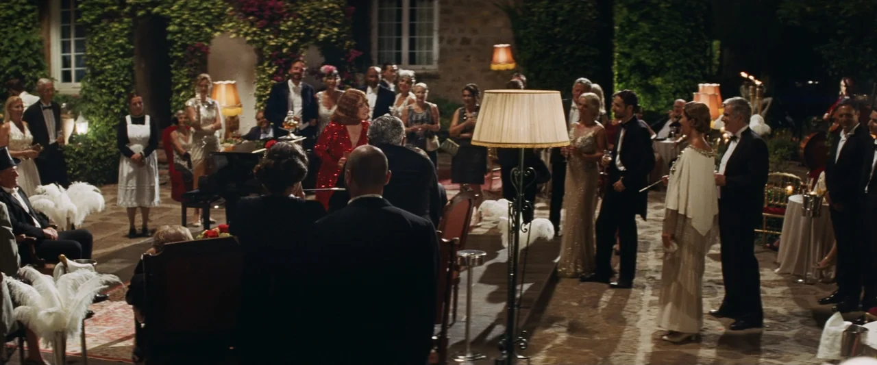 Masquerade (2022) movie still: wide — A stone courtyard at night is filled with people attending a formal garden party. Guests dressed in 1920s…